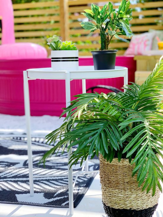 stock tank pool that is painted pink on a DIY deck with tropical rug and tropical plants